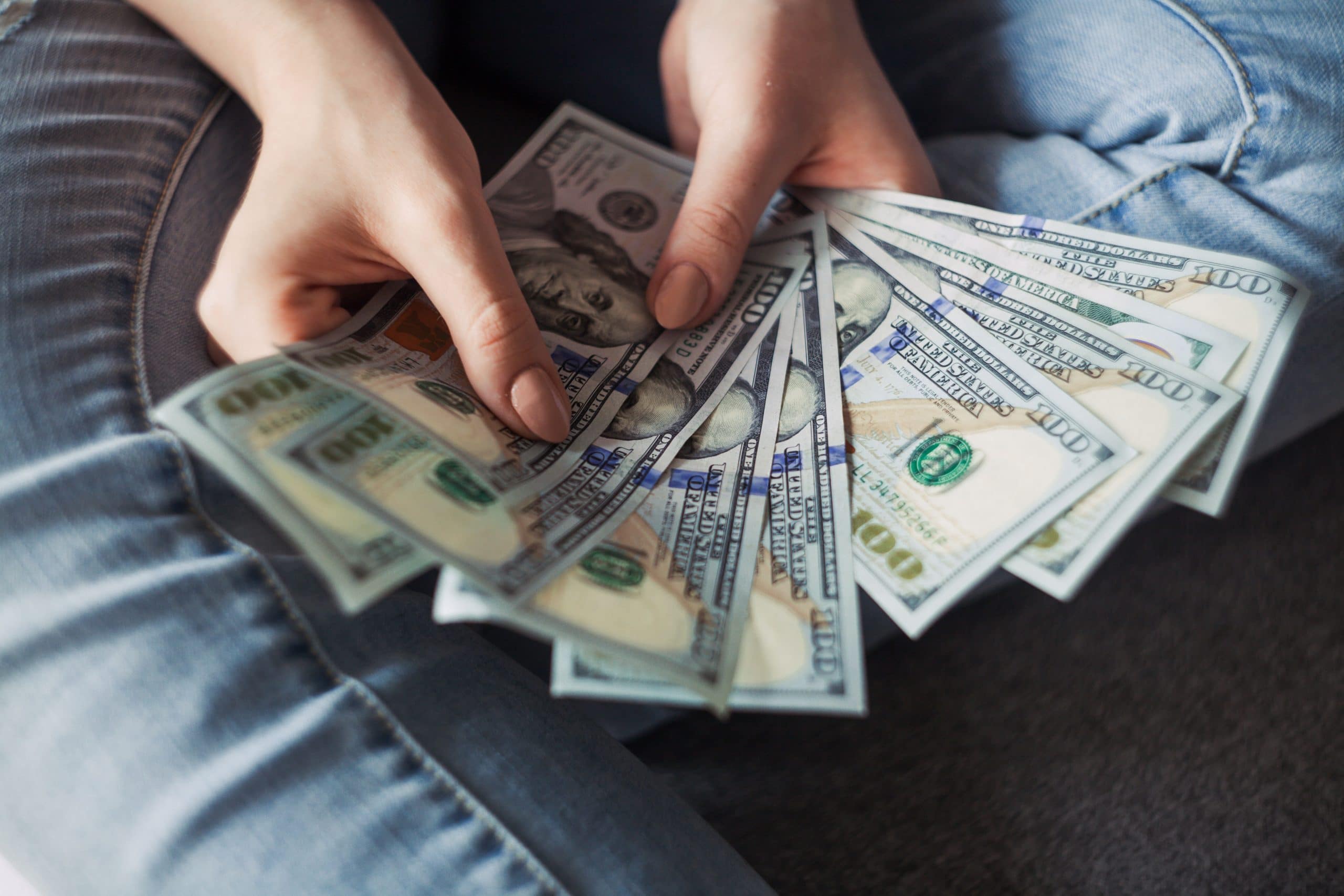 GIRL HOLDING HUNDRED DOLLAR BILLS IN HER HAND SITTING DOWN