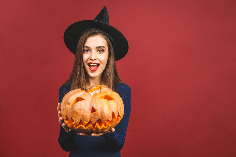 girl in a witch hat holding a jack-o-lantern