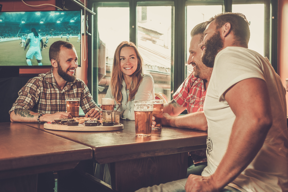 Men and women enjoy beer and company at a bar while watching soccer.