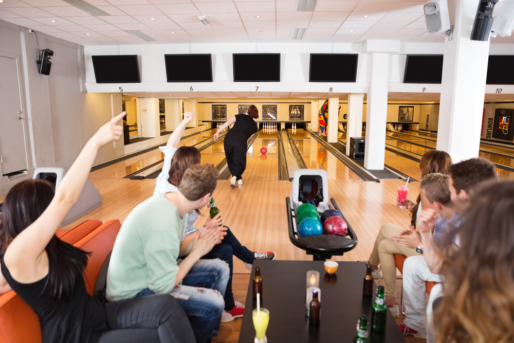 A group of young friends cheer their friend as she bowls.