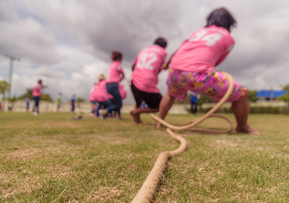 A group of people in pink jerseys play tug of war in a field.